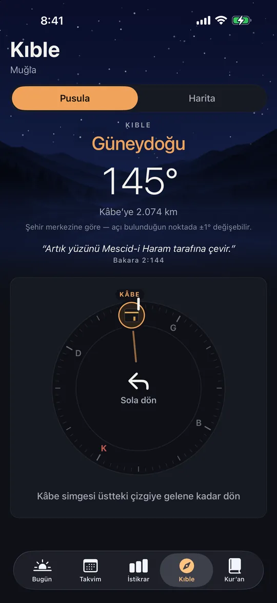 iPhone’da Kıble ekranı: Muğla’dan kıble güneydoğu, 145°, Kâbe’ye 2.074 km; pusulada Kâbe işareti ve «Sola dön» yönlendirmesi.